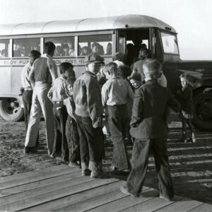 A historical photo from 1940 of schoolchildren lining up to board a school bus.