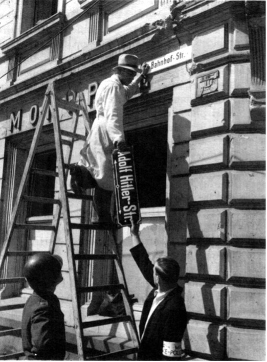 German civilians denazifying “Adolf Hitler Street” in Trier, Germany, while an American soldier watches (May, 1945)