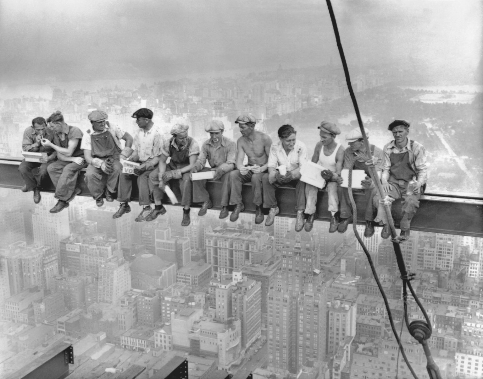 A group of men eating lunch together during work on a skyscraper beam over New York City