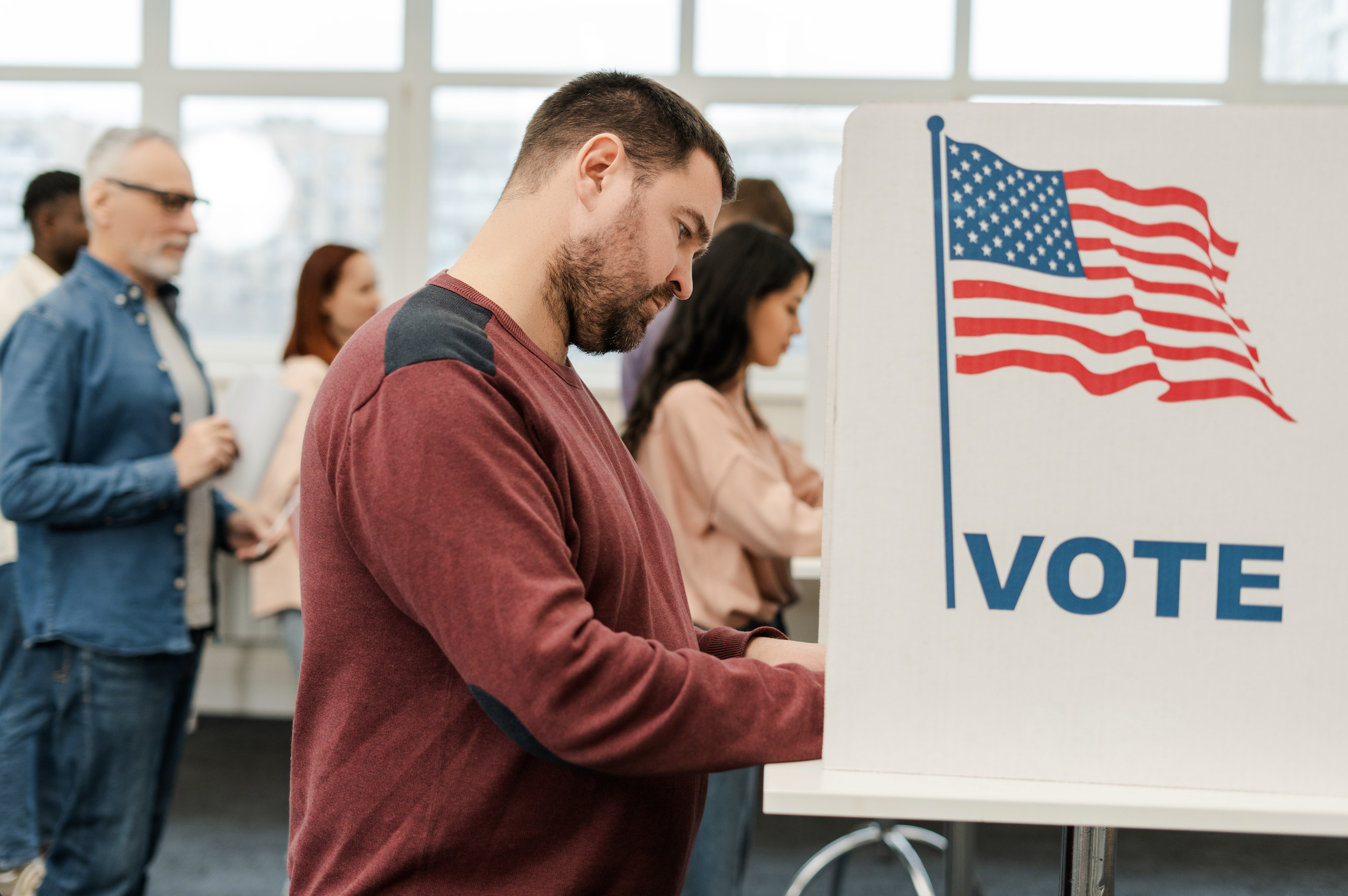 A man voting at poll station with others voting behind him