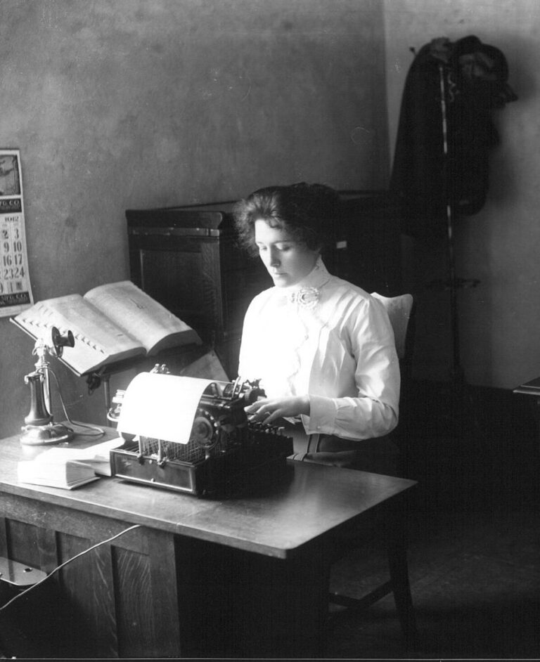 An antique photo of a woman in 1912 using a typewriter.